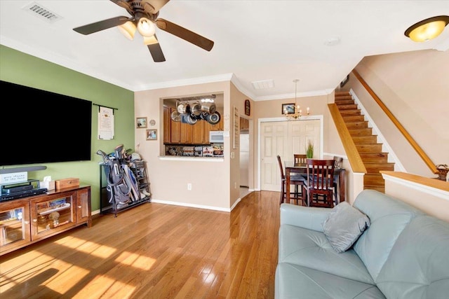 living area featuring stairway, crown molding, ceiling fan with notable chandelier, light wood-type flooring, and visible vents