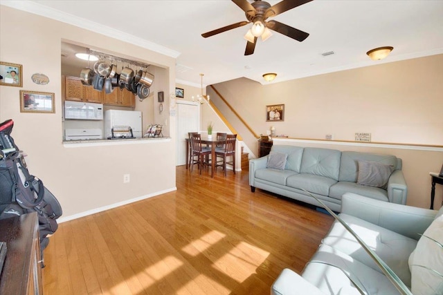 living room featuring baseboards, light wood-style flooring, crown molding, and ceiling fan with notable chandelier