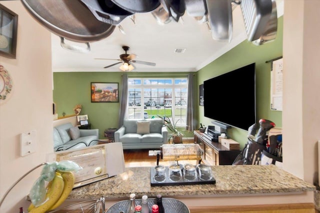 living room featuring a ceiling fan, visible vents, and crown molding