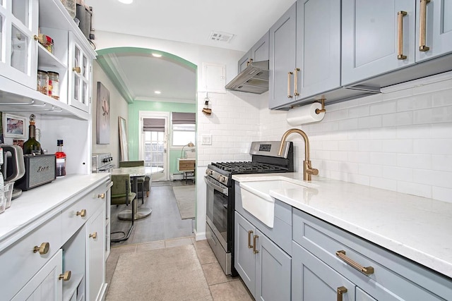 kitchen featuring under cabinet range hood, backsplash, visible vents, crown molding, and gas range