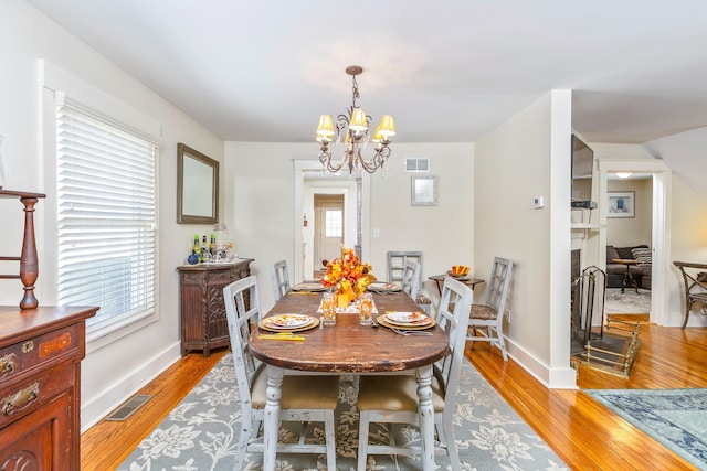 572A Montauk Hwy, Westhampton Beach, NY 11978 - dining room with light wood-type flooring, visible vents, an inviting chandelier, and a fireplace with raised hearth