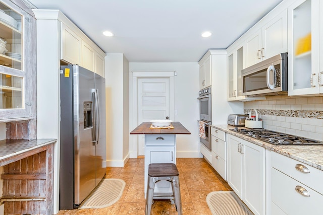 572A Montauk Hwy, Westhampton Beach, NY 11978 - kitchen featuring white cabinets, glass insert cabinets, backsplash, baseboards, and appliances with stainless steel finishes