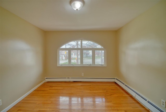 empty room with baseboard heating, light wood-type flooring, and baseboards