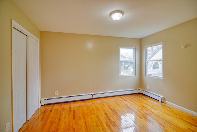 unfurnished room with a baseboard radiator, wood finished floors, and baseboards