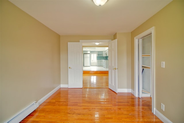 corridor featuring baseboard heating, light wood-type flooring, and baseboards