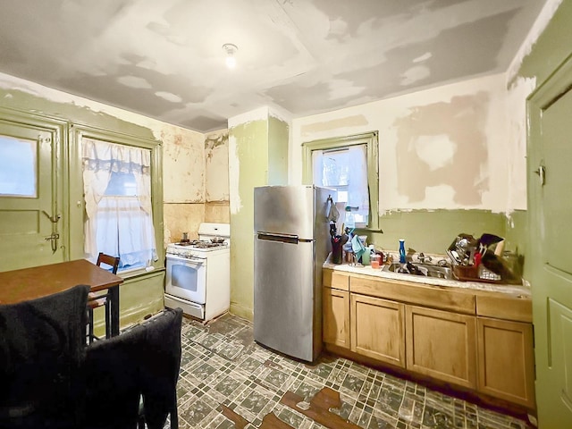 kitchen featuring white gas stove, freestanding refrigerator, plenty of natural light, and a sink