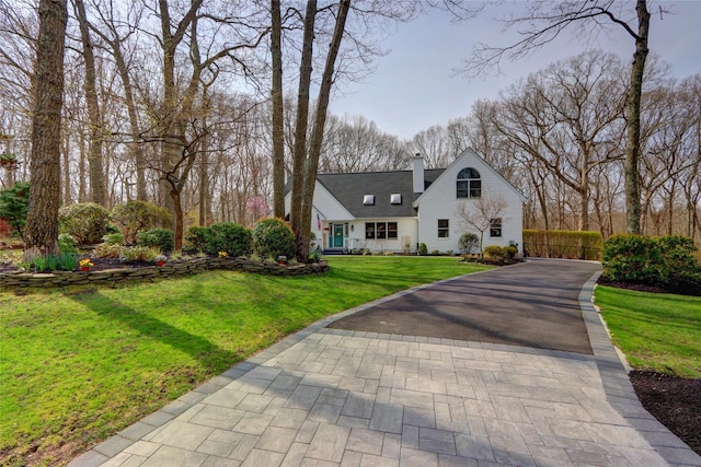 view of front of home with a front yard, a chimney, aphalt driveway, and fence
