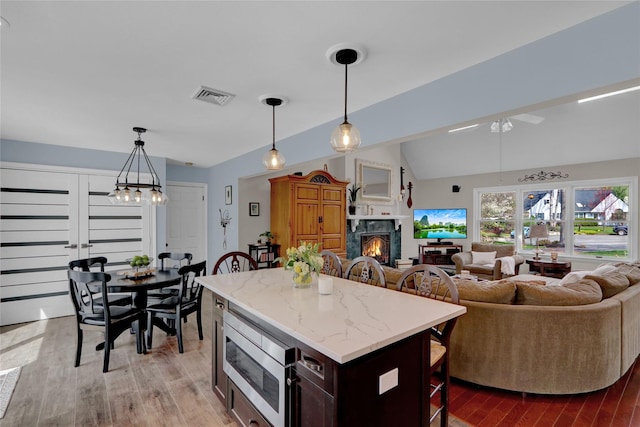 kitchen featuring stainless steel microwave, open floor plan, visible vents, a high end fireplace, and a breakfast bar area