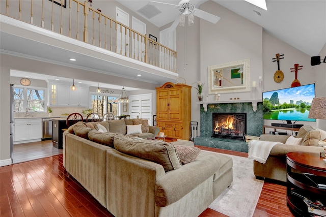 living area with high vaulted ceiling, hardwood / wood-style flooring, a ceiling fan, and a fireplace