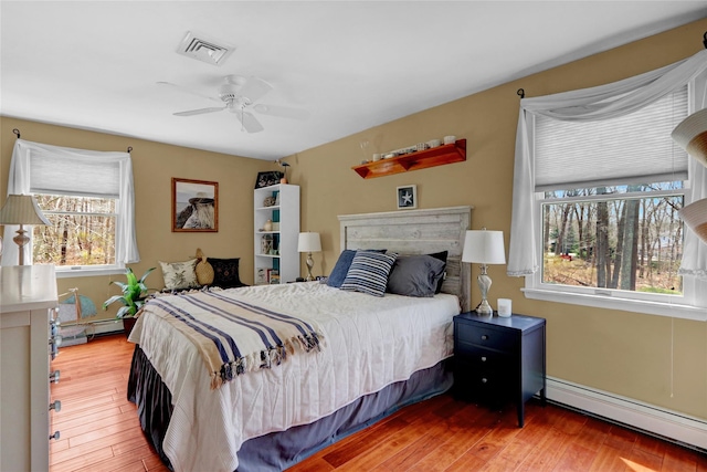 bedroom with wood finished floors, baseboard heating, and ceiling fan