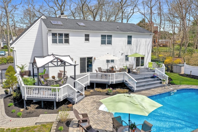 back of house with roof with shingles, a chimney, a wooden deck, outdoor dining area, and an outdoor pool