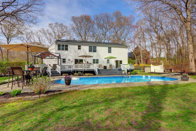 rear view of house with fence, a wooden deck, an outdoor pool, and a yard
