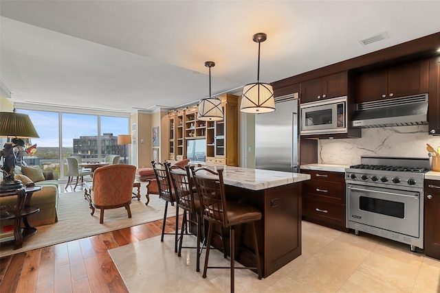 kitchen featuring built in appliances, a breakfast bar area, under cabinet range hood, a kitchen island, and tasteful backsplash