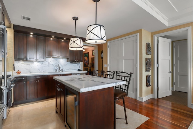 kitchen with baseboards, visible vents, a sink, a kitchen island, and tasteful backsplash