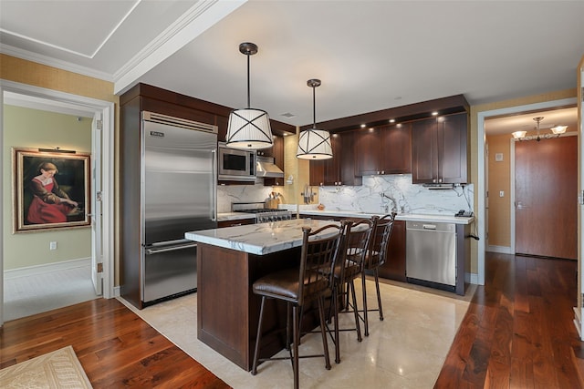 kitchen with built in appliances, decorative backsplash, a center island, and dark brown cabinets