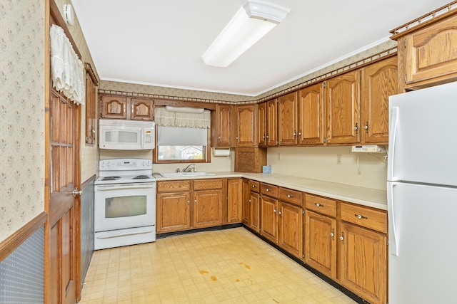 kitchen featuring brown cabinetry, wallpapered walls, a sink, and white appliances