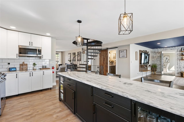 kitchen featuring hanging light fixtures, stainless steel appliances, dark cabinetry, white cabinets, and light stone countertops
