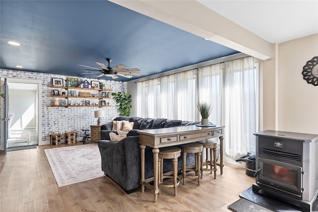 living room featuring a ceiling fan, a wood stove, and wood finished floors