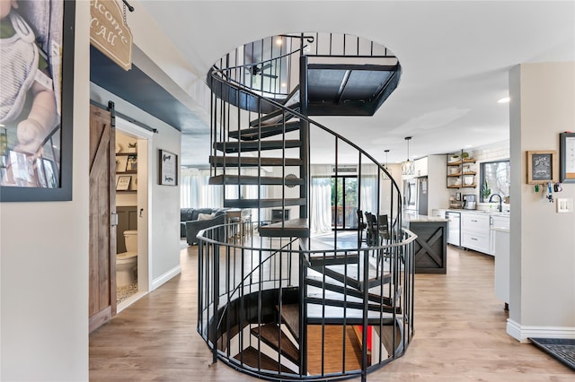 stairway featuring wood finished floors, baseboards, a wealth of natural light, and a barn door