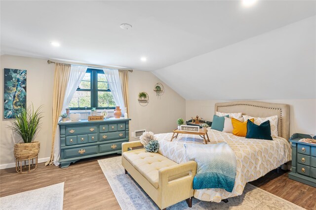 bedroom with vaulted ceiling, wood finished floors, visible vents, and baseboards