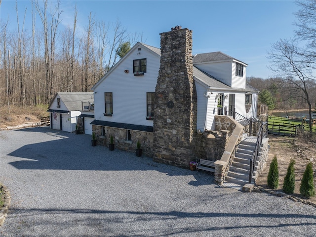 view of home's exterior featuring a detached garage, a shingled roof, a chimney, and fence
