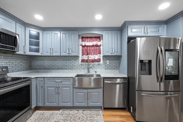 kitchen featuring glass insert cabinets, a sink, stainless steel appliances, gray cabinets, and decorative backsplash