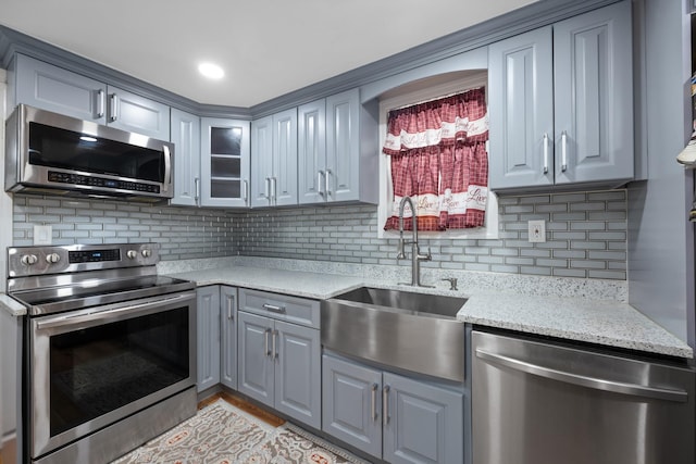 kitchen with gray cabinets, decorative backsplash, a sink, and stainless steel appliances