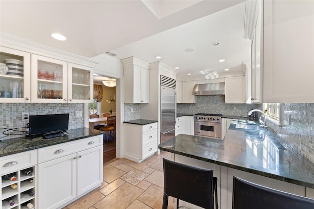 kitchen featuring a sink, wall chimney range hood, white cabinetry, decorative backsplash, and high end appliances