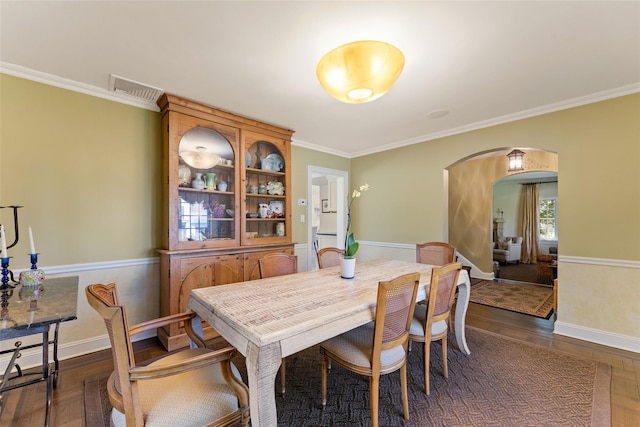 dining room featuring baseboards, ornamental molding, visible vents, dark wood-type flooring, and arched walkways