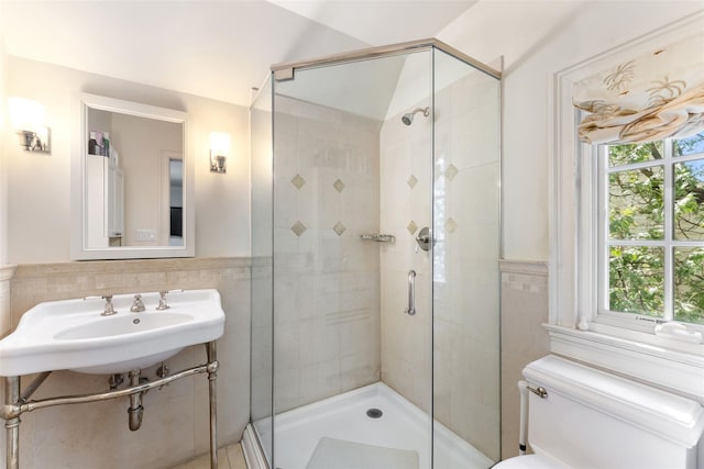 bathroom with toilet, tile walls, a shower stall, and a wainscoted wall