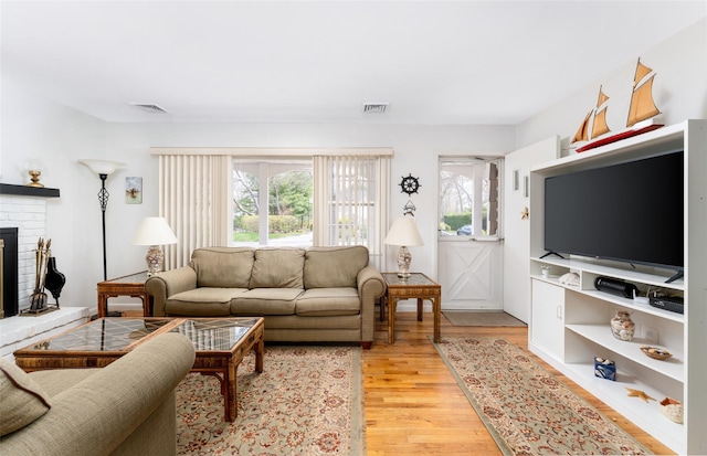 living room featuring visible vents, a brick fireplace, light wood finished floors, and plenty of natural light