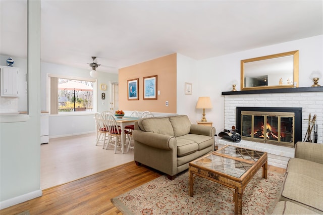 living room featuring a fireplace, ceiling fan, light wood finished floors, and baseboards