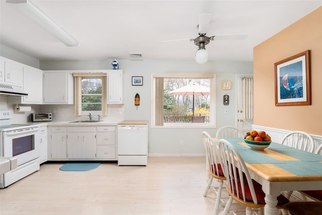 kitchen with light wood finished floors, a sink, under cabinet range hood, white appliances, and light countertops