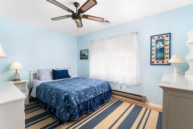 bedroom with wood finished floors, a baseboard heating unit, ceiling fan, baseboards, and visible vents
