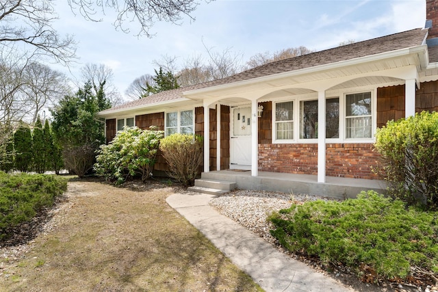 ranch-style house featuring a porch, a shingled roof, and brick siding