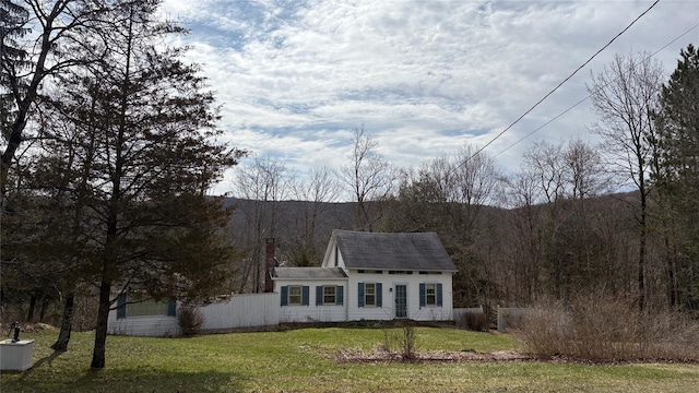 view of front facade with a view of trees, a chimney, a front yard, and fence
