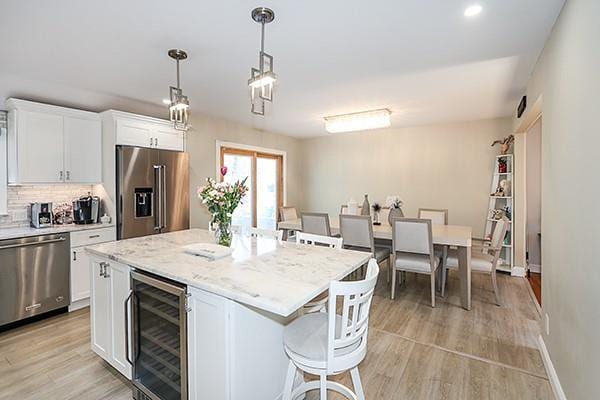 80 Lauren Ave, Dix Hills, NY 11746 - kitchen featuring appliances with stainless steel finishes, wine cooler, white cabinets, light wood-style flooring, and tasteful backsplash