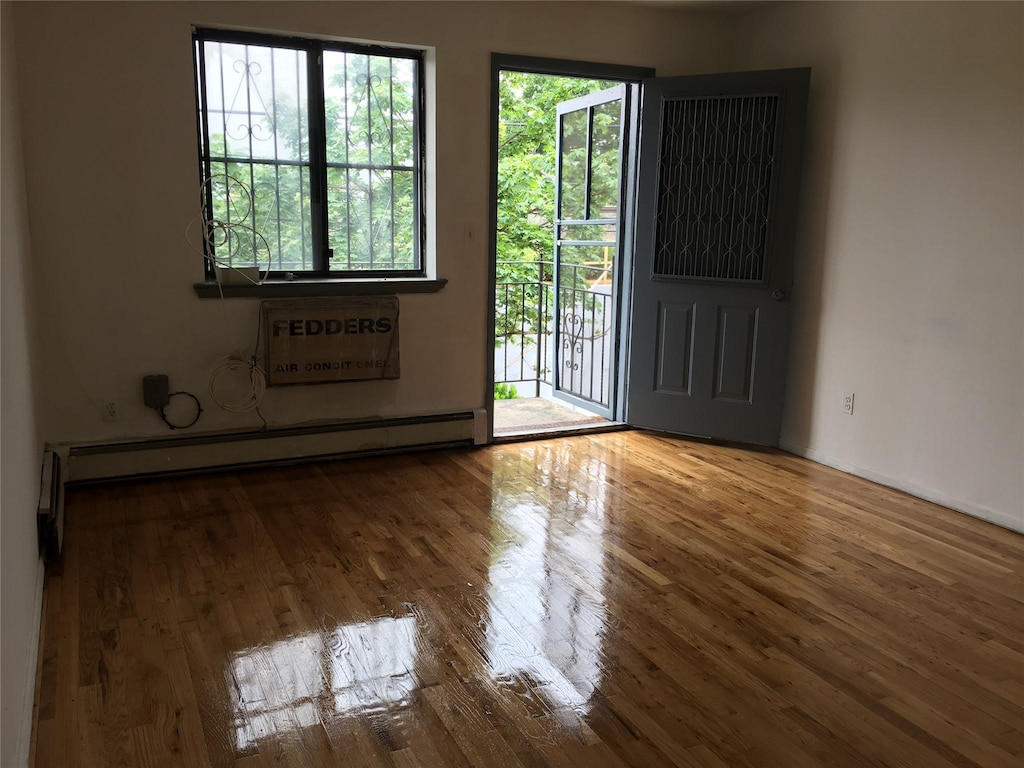 unfurnished room featuring baseboards, wood finished floors, and a baseboard radiator