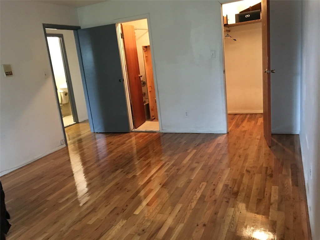 unfurnished bedroom featuring a closet, baseboards, wood finished floors, and a walk in closet