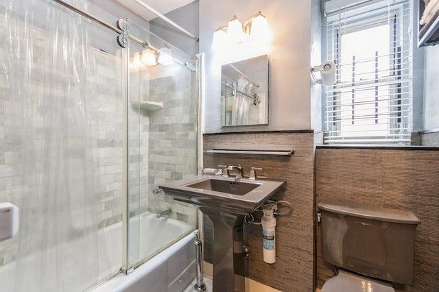 bathroom with toilet, tile walls, and bath / shower combo with glass door