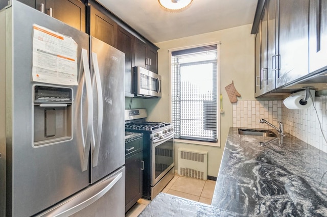 kitchen with dark stone countertops, light tile patterned floors, stainless steel appliances, radiator, and a sink