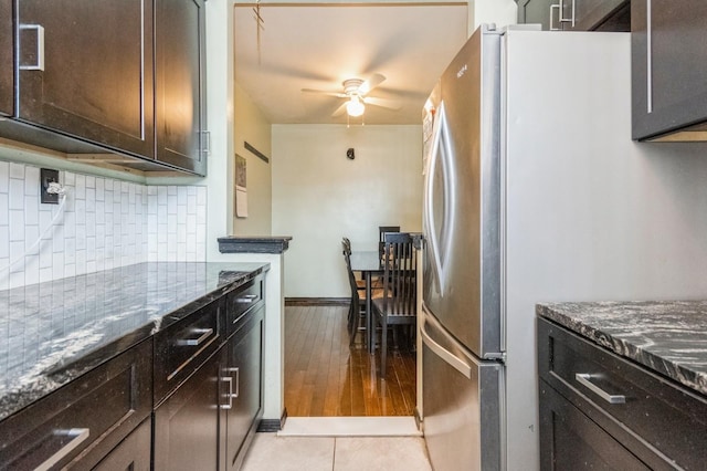 kitchen featuring dark stone counters, tasteful backsplash, dark brown cabinets, freestanding refrigerator, and a ceiling fan