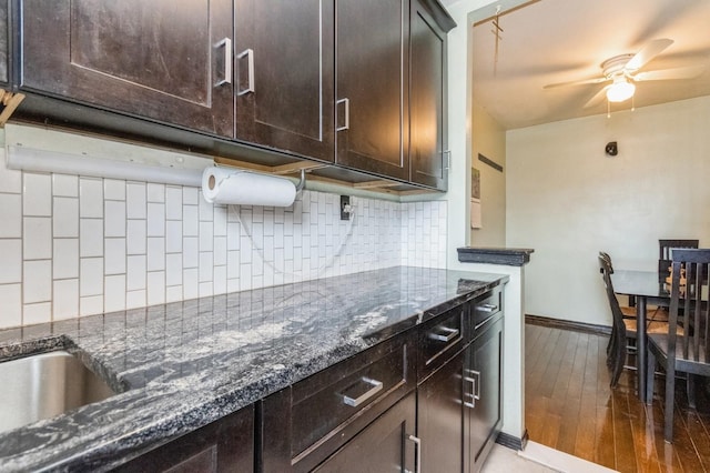kitchen featuring dark stone counters, tasteful backsplash, baseboards, dark brown cabinetry, and a ceiling fan