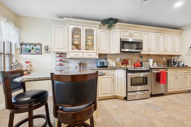 60 Southgate Cir, Massapequa Park, NY 11762 - kitchen featuring stainless steel appliances, a breakfast bar, cream cabinetry, and tasteful backsplash
