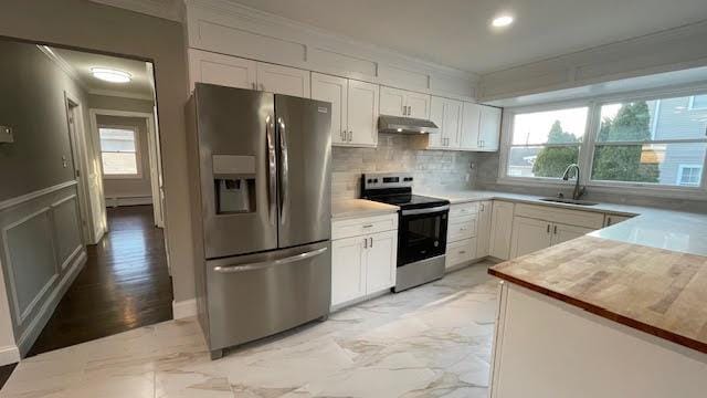 kitchen featuring appliances with stainless steel finishes, a sink, backsplash, under cabinet range hood, and ornamental molding
