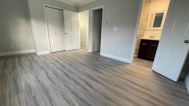 unfurnished bedroom with crown molding, a closet, wood finished floors, baseboards, and ensuite bathroom