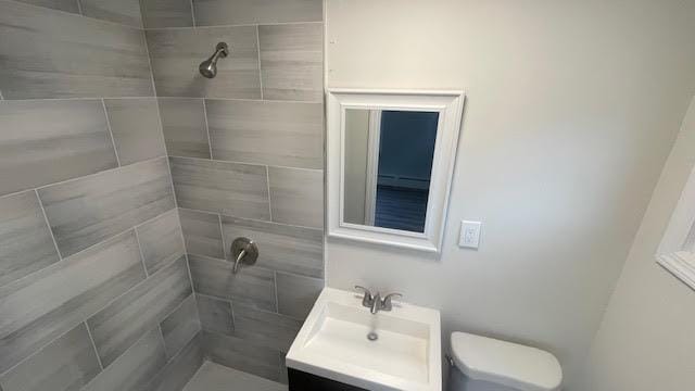 full bath with vanity, a tile shower, and toilet