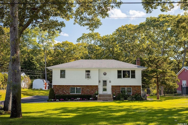 raised ranch featuring entry steps, a chimney, a front lawn, and brick siding