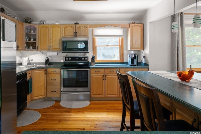 kitchen featuring stainless steel appliances, light wood-style floors, a sink, and decorative backsplash