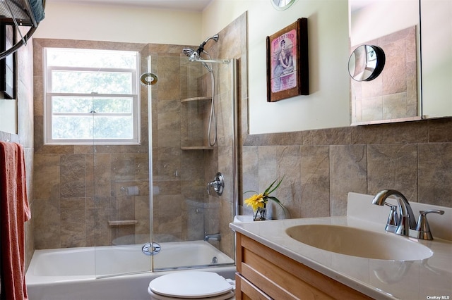 bathroom featuring tile walls, toilet, vanity, and shower / bath combination with glass door